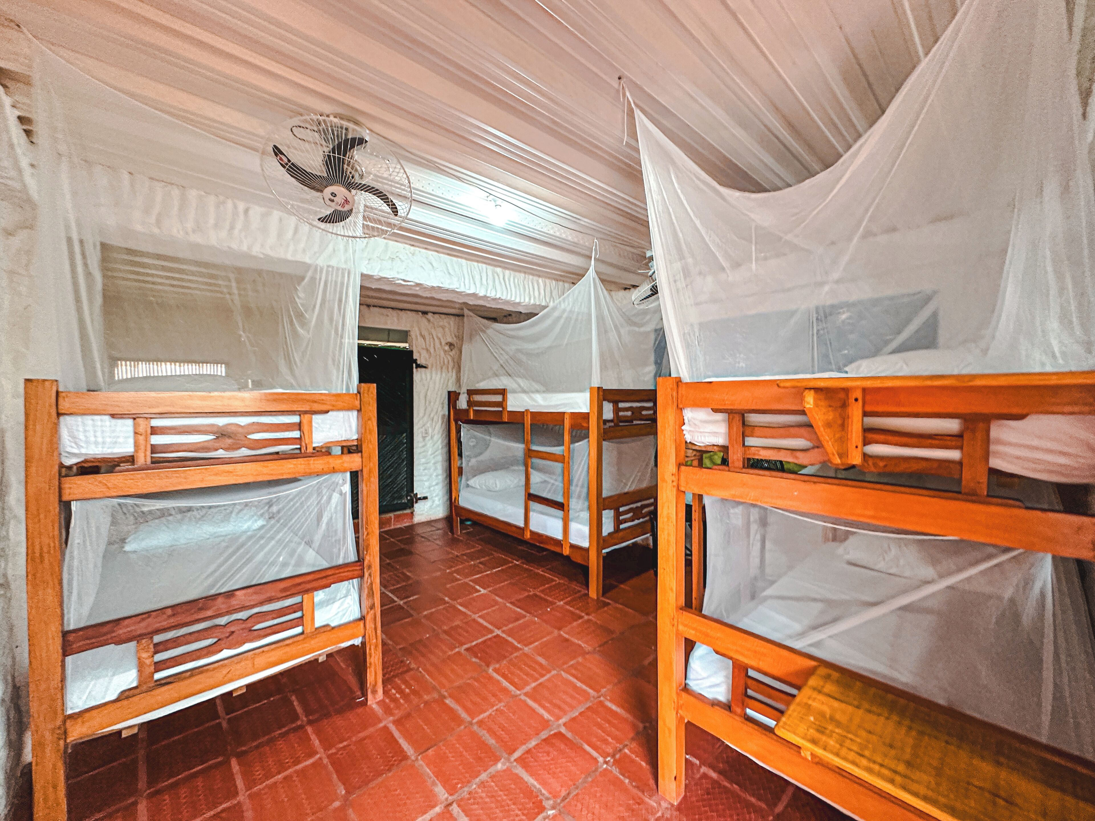 A room with bunk beds, mosquito nets, and a ceiling fan.