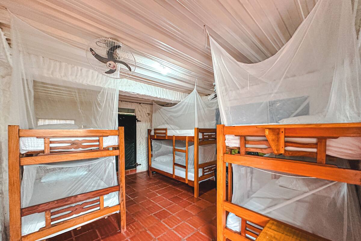 A room with bunk beds, mosquito nets, and a ceiling fan.