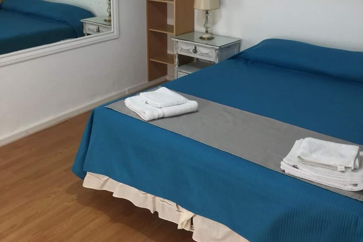 A hotel room with a bed, a nightstand, a mirror, and a wooden shelf unit.
