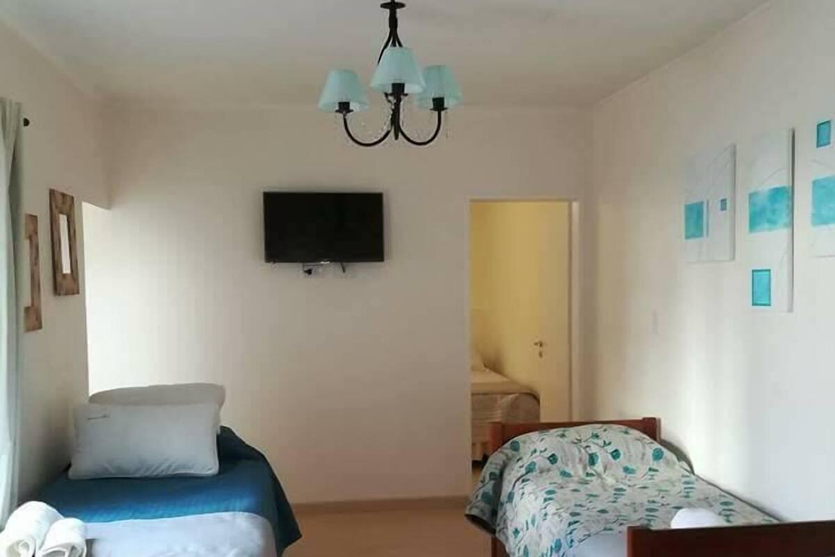 A room with two beds, a TV mounted on the wall, and a chandelier.
