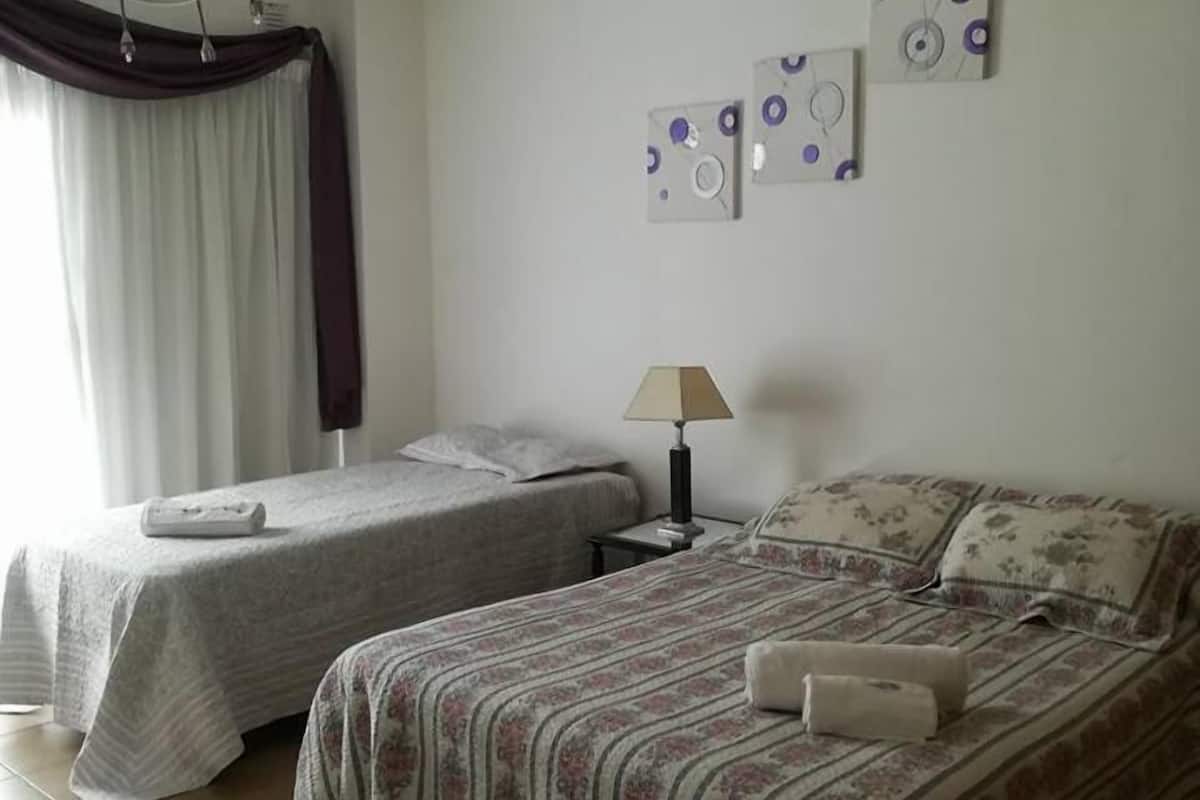 A bedroom with two single beds, a nightstand, a lamp, and a ceiling fan.
