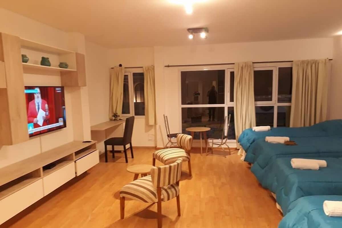 A hotel room with a TV, a desk, a chair, a small table, a sofa, and a window.