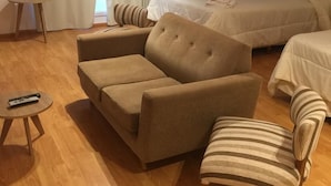 Ett hotellrum med en soffa, en fåtölj och en säng. Det finns ett litet bord med en fjärrkontroll på.