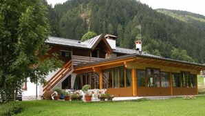 A wooden chalet with a covered porch, a staircase, and a mountain backdrop. - La Vecchia Latteria (Pontebba)