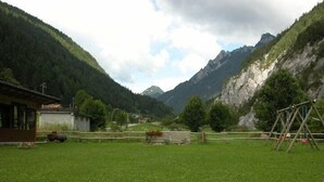 A rural landscape with a grassy field, a wooden fence, a small building, and mountains in the background. - La Vecchia Latteria (Pontebba)