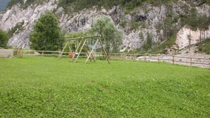 A grassy field with a wooden swing set and a wooden fence. - La Vecchia Latteria (Pontebba)
