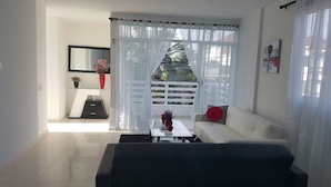 A modern living room with a sofa, a coffee table, and a TV. There is a window with curtains, a small table with a vase, and a mirror on the wall. - Caribbean Sea Breeze (San Andrés)