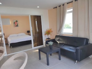 A hotel room with a bed, a sofa, a small table, and a potted plant.