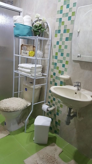 A bathroom with a toilet, sink, and a shelf with towels and toiletries.