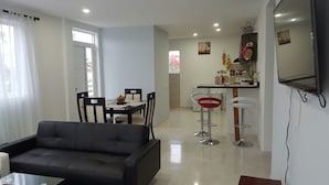A modern living room with a black sofa, dining table, and chairs. There is a kitchen area with a refrigerator, sink, and bar stools. - Caribbean Sea Breeze (San Andrés)