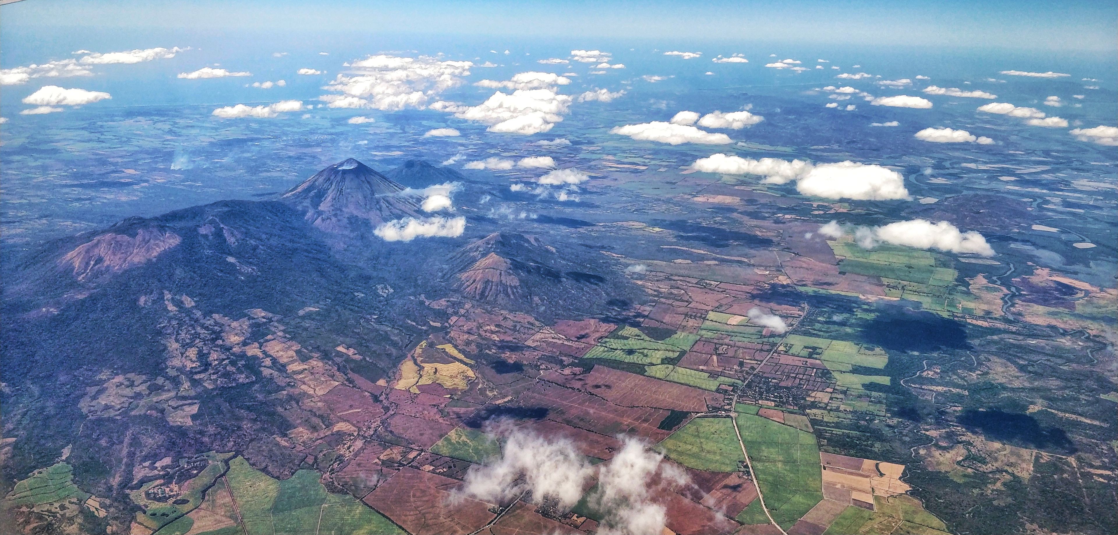 An aerial view of a mountainous landscape with fields and scattered clouds.
