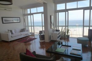 Un salon spacieux avec un canapé blanc, une table basse et une vue sur la plage grâce à de grandes fenêtres.