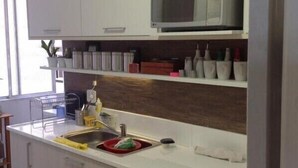 A modern kitchen with white cabinetry, a stainless steel sink, and a microwave. There are shelves above the sink holding various kitchen items and decorative objects. - Vista Espetacular Copacabana (Rio de Janeiro)
