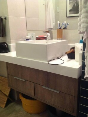 Une salle de bain avec un lavabo blanc, un meuble en bois et un seau jaune.