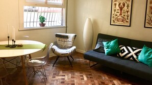 A room with a dining table, a sofa, a chair, a window with bars, and two framed botanical prints on the wall. - Leblon 2 Quartos 500 Metros da Praia (Rio de Janeiro)