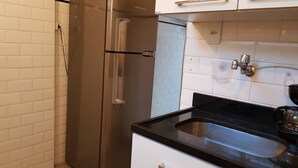 A kitchen with a stainless steel refrigerator, white cabinets, a black countertop, and a sink. - Leblon 2 Quartos 500 Metros da Praia (Rio de Janeiro)