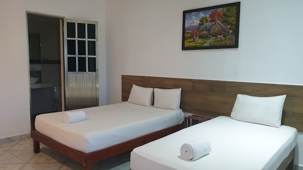 Une chambre d’hôtel avec deux lits simples, une tête de lit en bois, un tableau au mur et une salle de bain visible à travers une porte ouverte.