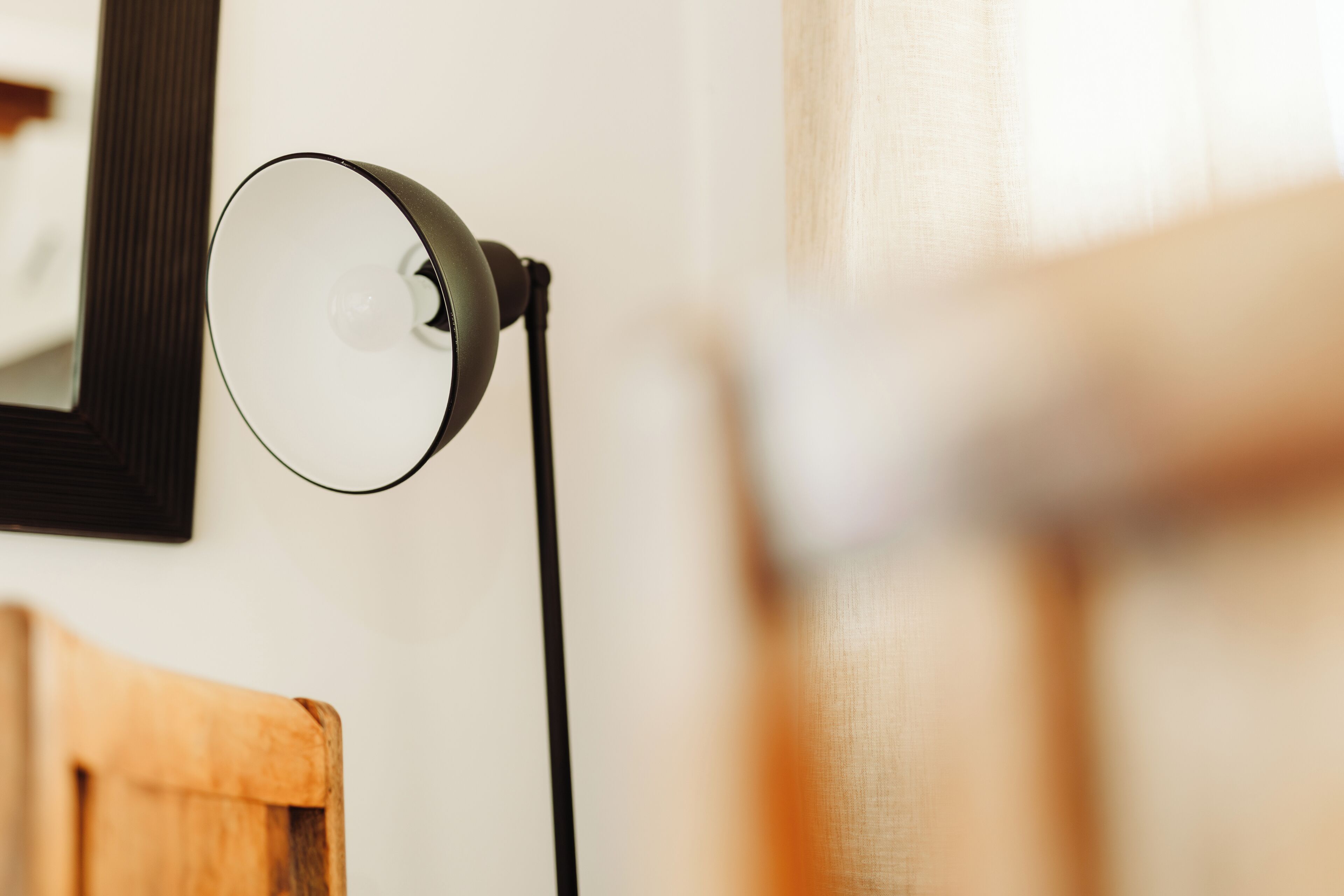 A lamp with a black base and a white shade, positioned on a white wall.