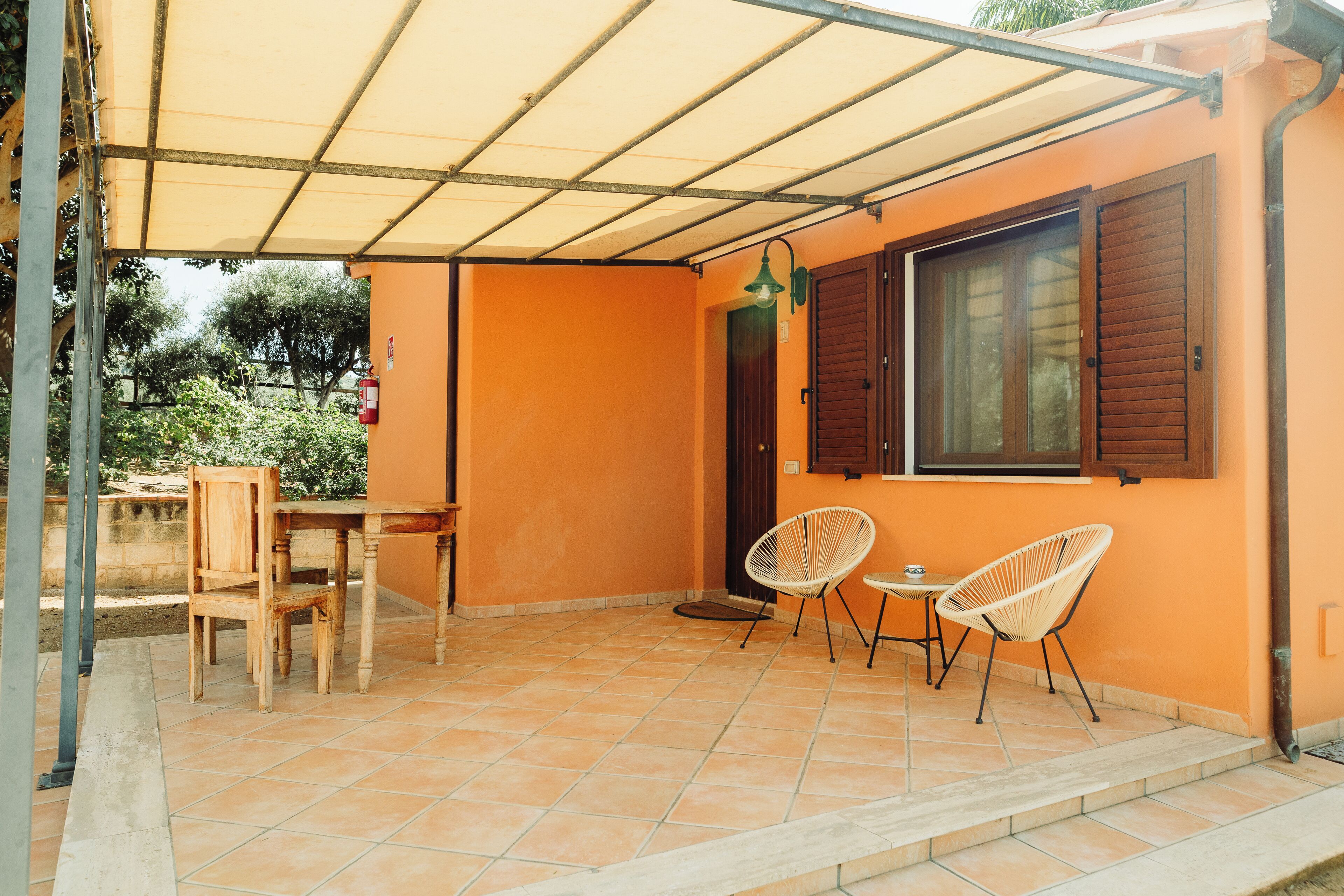 A covered patio area with a table and chairs, a door, and a window with shutters.
