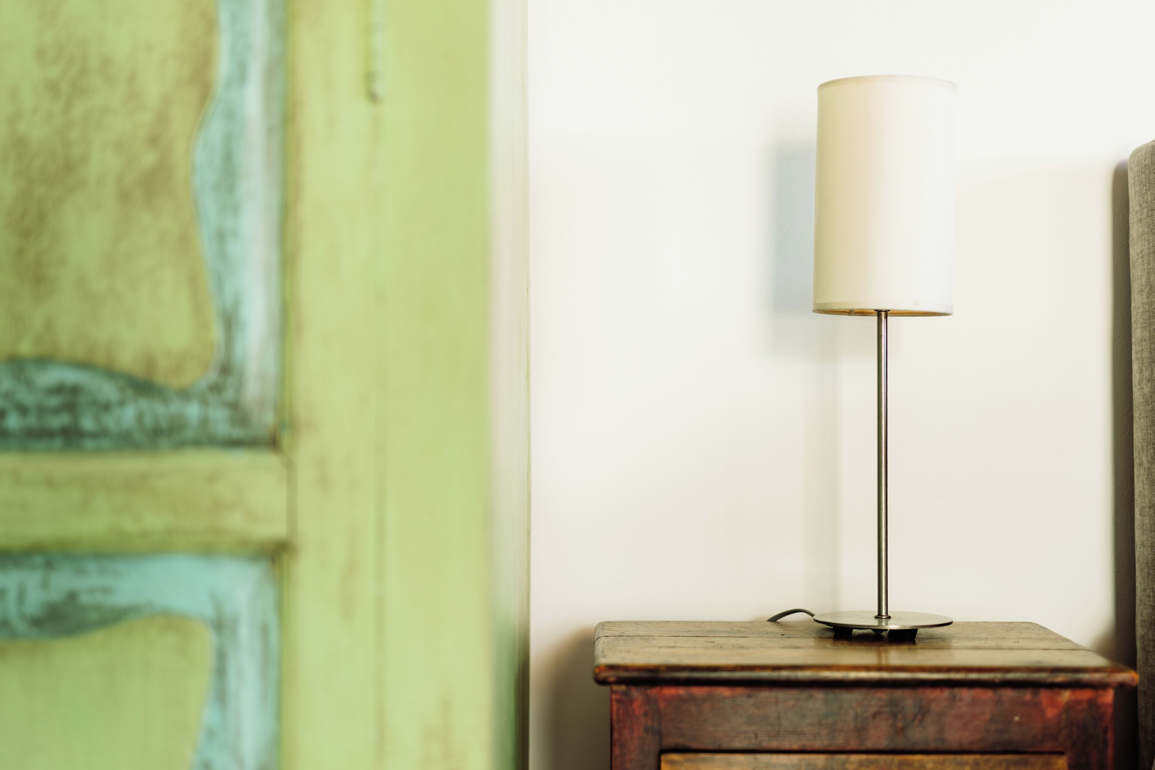 A lamp on a wooden nightstand against a wall with a green and white color scheme.