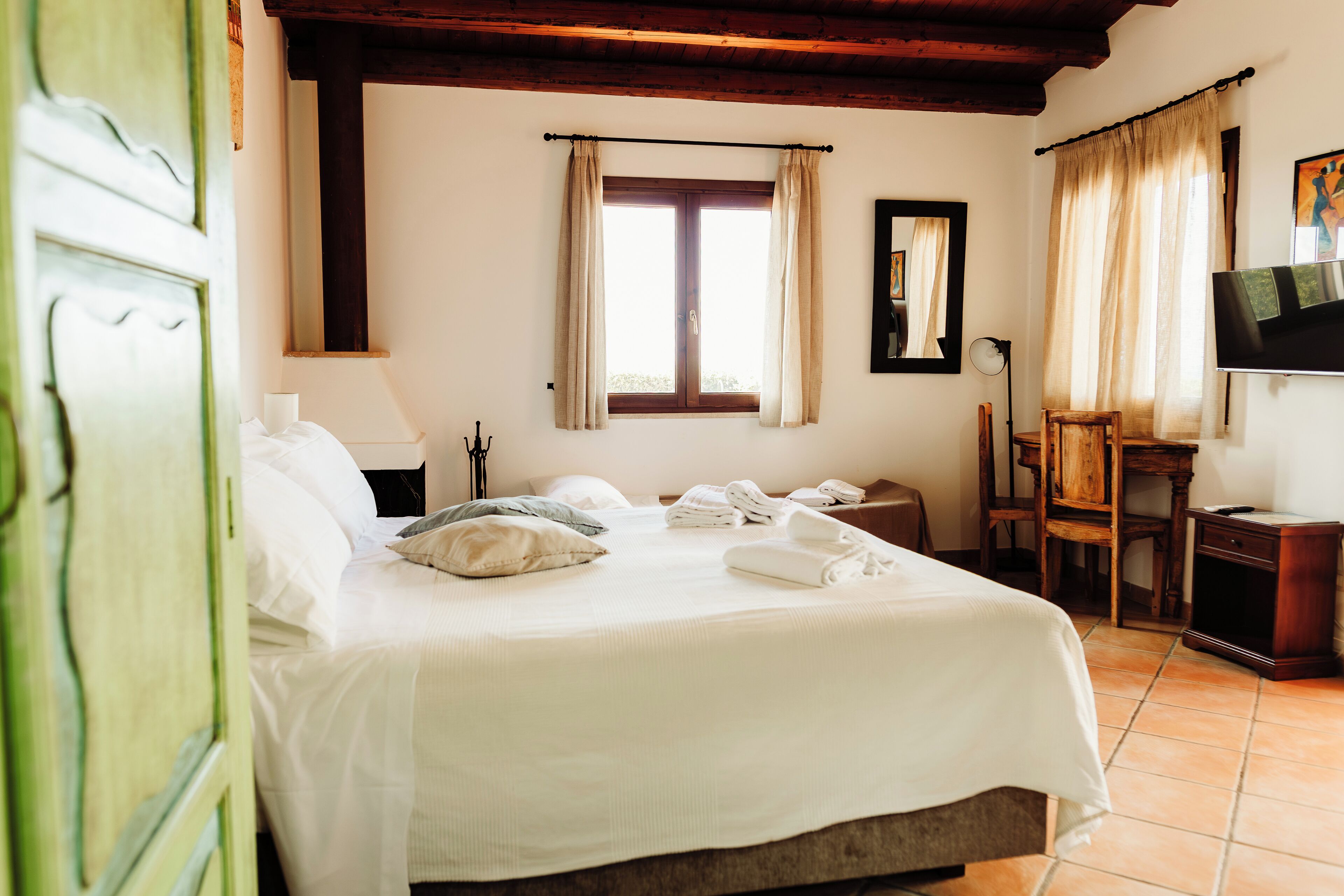 Une chambre d’hôtel avec un lit, un bureau, une chaise, une télévision et une fenêtre avec des rideaux.