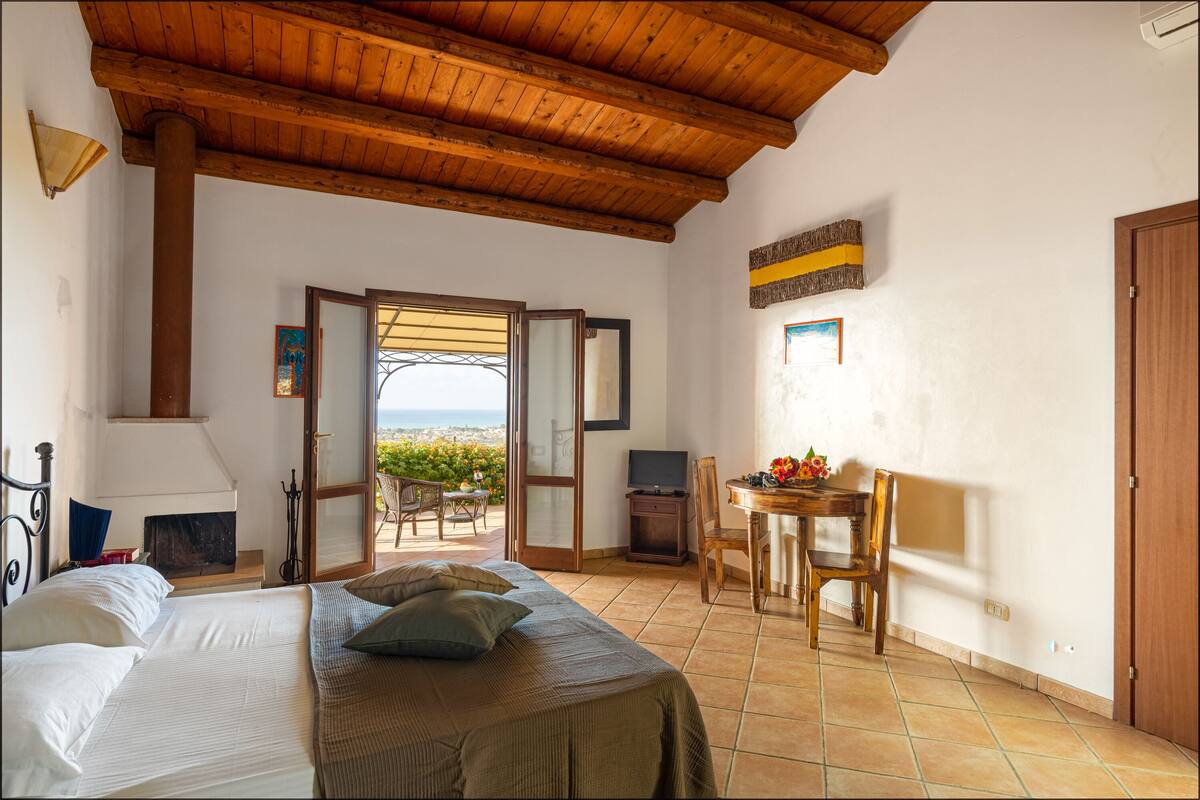 A bedroom with a bed, a desk, and a view of the sea.