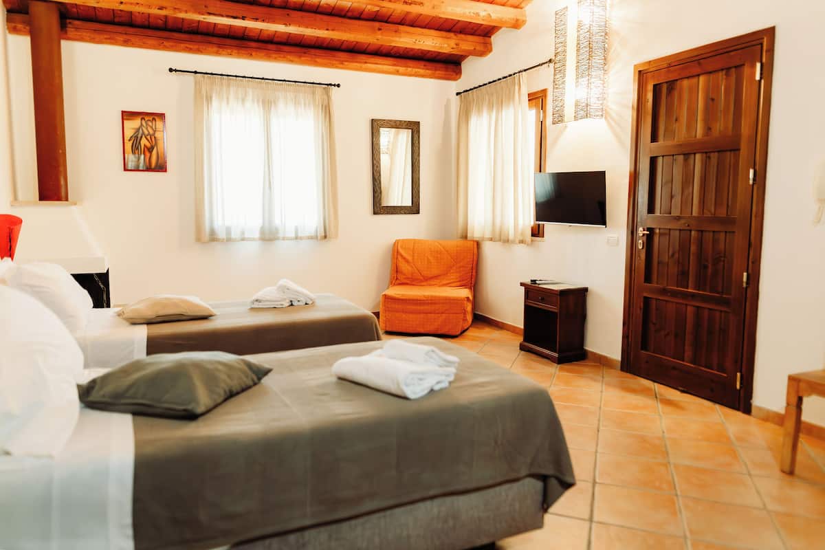 A hotel room with two beds, a television, a wooden door, and a window with curtains.