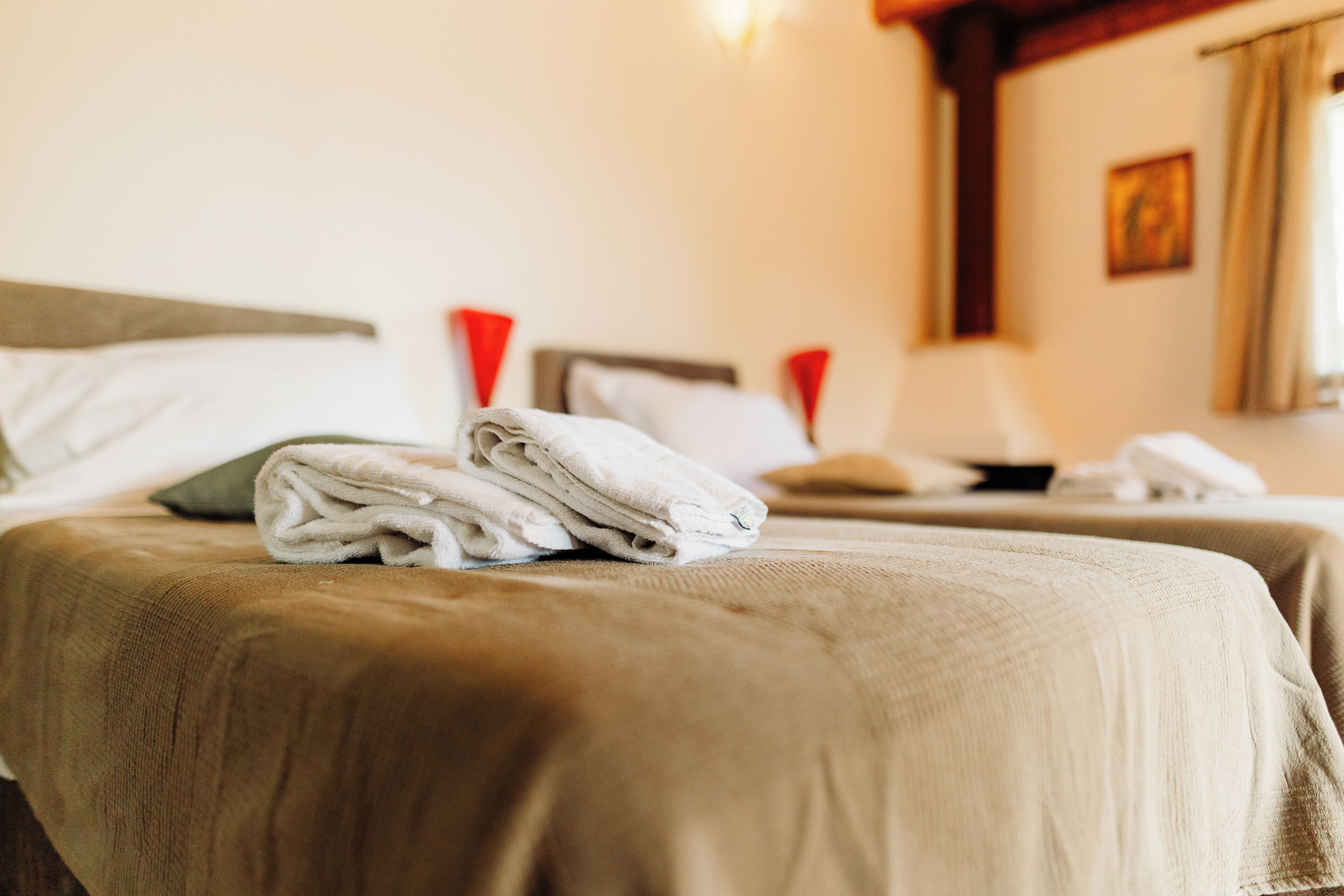 Une chambre d’hôtel avec deux lits, chacun recouvert d’une couverture marron et agrémenté d’oreillers blancs. Une serviette blanche pliée est posée sur le lit de gauche.