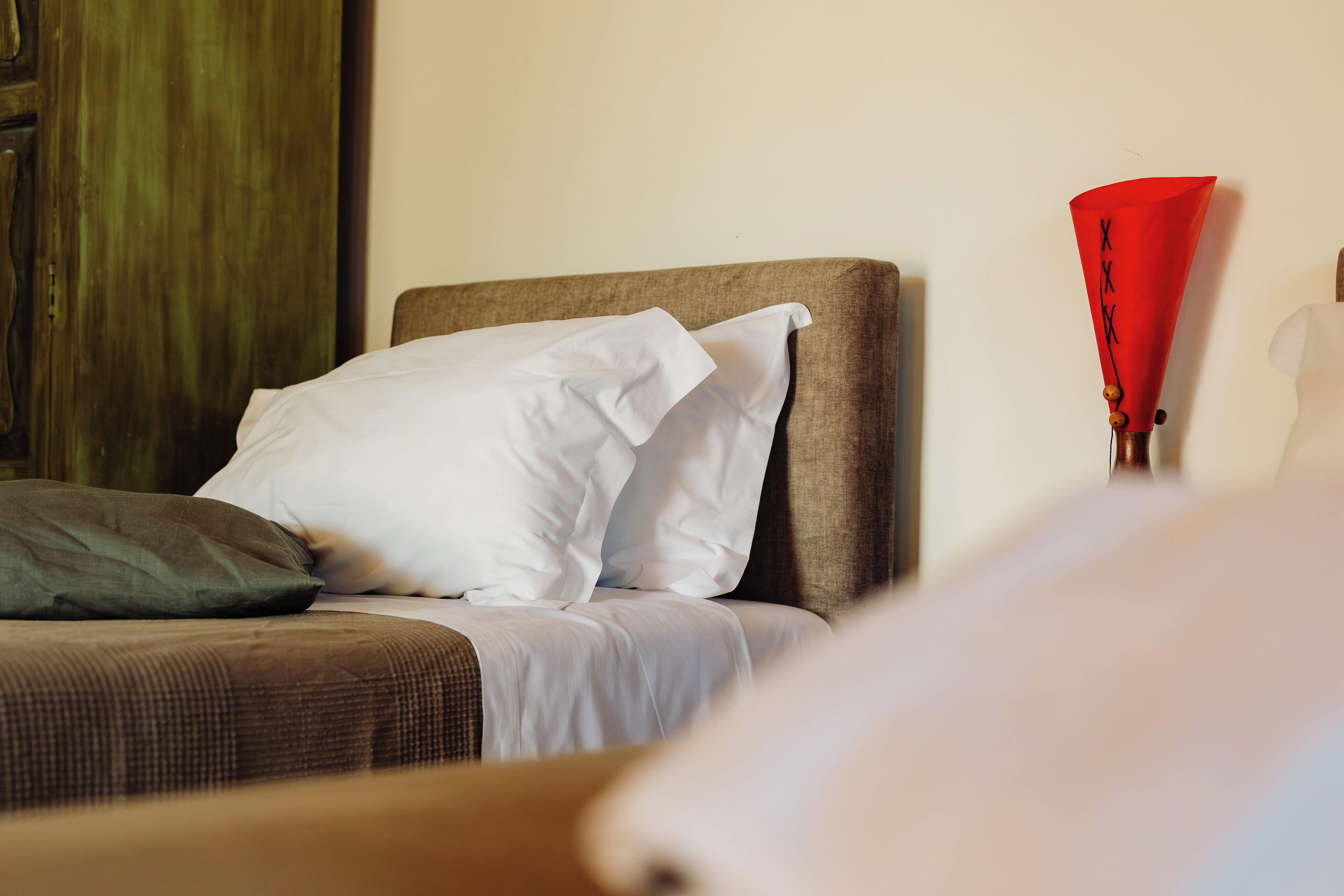 Una cama con almohadas blancas y verdes, un cabecero marrón y un objeto rojo a la derecha.