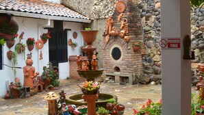 A courtyard with a fountain, terracotta pots, and a stone wall. - Hospedaje el Mirador (Villa de Leyva)