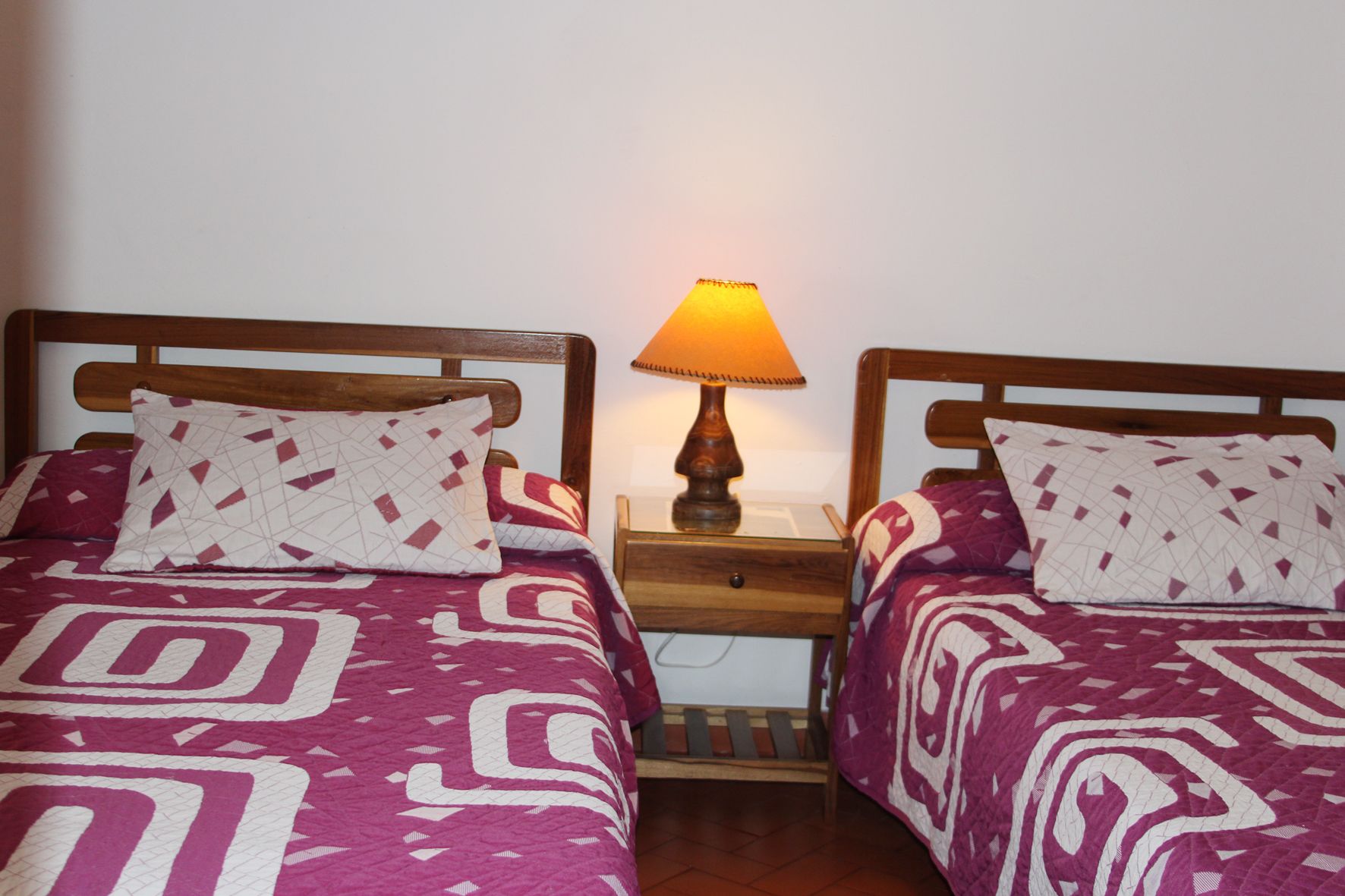 Two beds with patterned bedding, a nightstand with a lamp, and a wooden headboard.