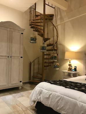 Un dormitorio con una escalera de caracol, una cama, una mesita de noche, una lámpara y un armario.