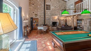 A cozy room with a pool table, a fireplace, and a stone wall. - Aux Chambres des Bujours (Saint-Georges-des-Coteaux)