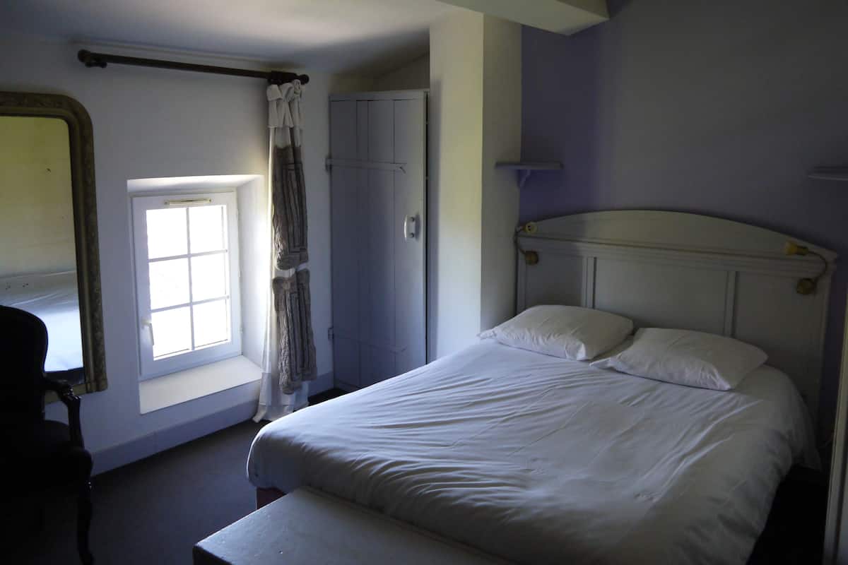 A bedroom with a single bed, a window with a view, a door, and a mirror.