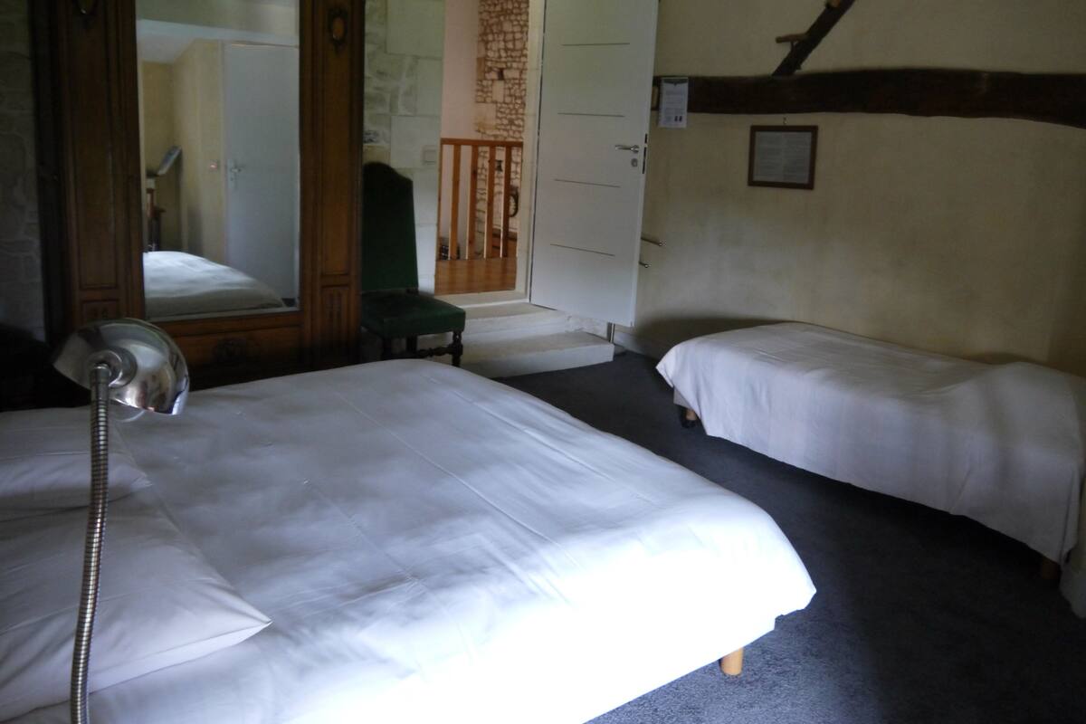 A room with two single beds, a wooden wardrobe, a mirror, and a green chair.