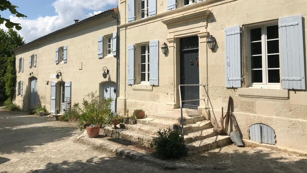 A two-story building with light-colored stone walls and blue shutters. There are steps leading to the entrance, and potted plants are placed at the base. - Aux Chambres des Bujours (Saint-Georges-des-Coteaux)