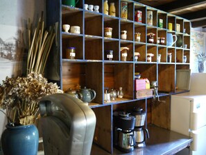Eine Küche mit Holzböden, die verschiedene Gläser und Behälter beherbergen. Auf einem Tisch steht eine blaue Vase mit Trockenblumen und auf der Arbeitsplatte ein Kaffeeautomat.