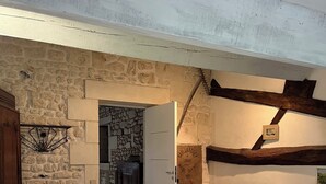 A rustic room with two beds, a wooden bench, a stone wall, and a door leading to another room. - Aux Chambres des Bujours (Saint-Georges-des-Coteaux)