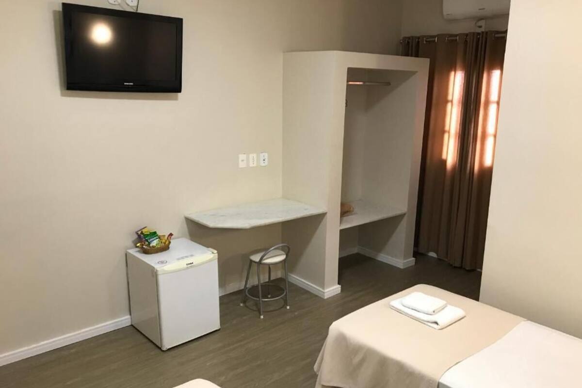 Een hotelkamer met een bed, een klein bureau, een stoel, een televisie en een raam met gordijnen.