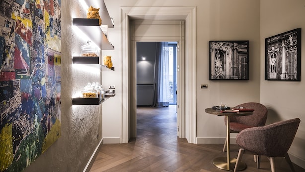 A hallway with a modern interior, featuring a wooden floor, a wall with abstract art, a shelf with decorative items, and a dining area with a table and chairs. - inCanto (Palermo)