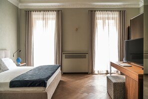 A hotel room with a bed, a desk with a TV, and a heater.