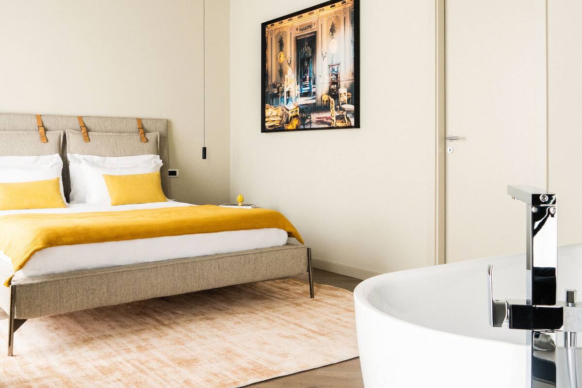 Une chambre à coucher moderne avec un grand lit, une baignoire blanche et un tableau accroché au mur.