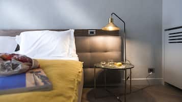 Un lit bien fait, avec des oreillers blancs et une couverture jaune, une table de chevet avec une lampe, et une petite table sur laquelle se trouvent un verre et un fruit.