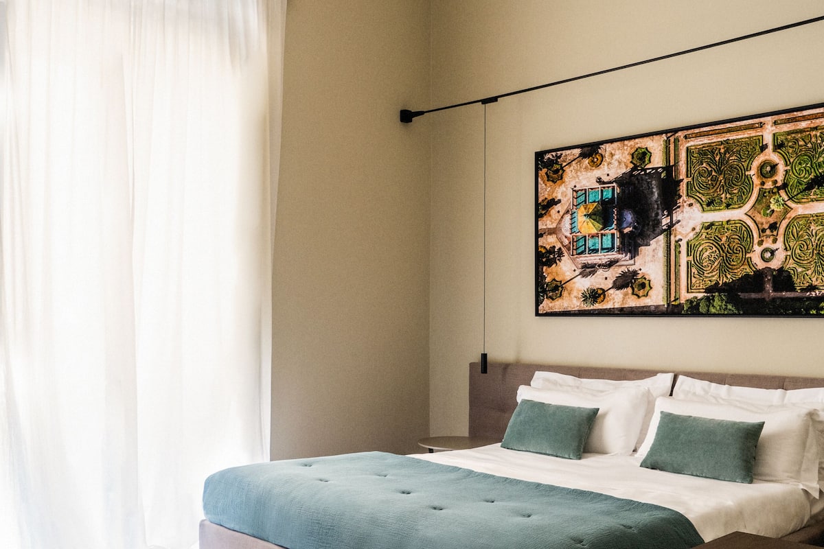 Une chambre à coucher avec un lit, un pouf vert et une œuvre d’art accrochée au mur.