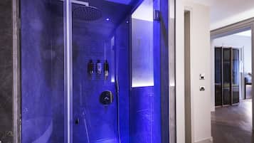 Une salle de bain moderne avec une douche à parois de verre, une pomme de douche visible et une petite étagère contenant des articles de toilette.