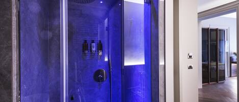 Un baño moderno con cabina de ducha de vidrio, ducha expuesta y una pequeña repisa con artículos de aseo.