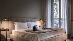 A neatly made bed with white linens, a bedside table with a lamp, and a view of a statue through the window. - inCanto (Palermo)
