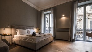A modern bedroom with a large bed, a bedside table with a lamp, and a view of the city through large windows. - inCanto (Palermo)