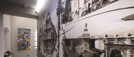 A hallway with a large mural of a historical scene, a modern abstract painting, and a wooden floor.