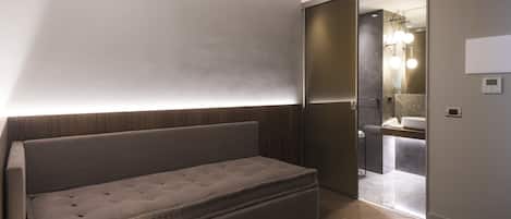 A modern room with a sofa, a mirror, and a bathroom visible through an open door.